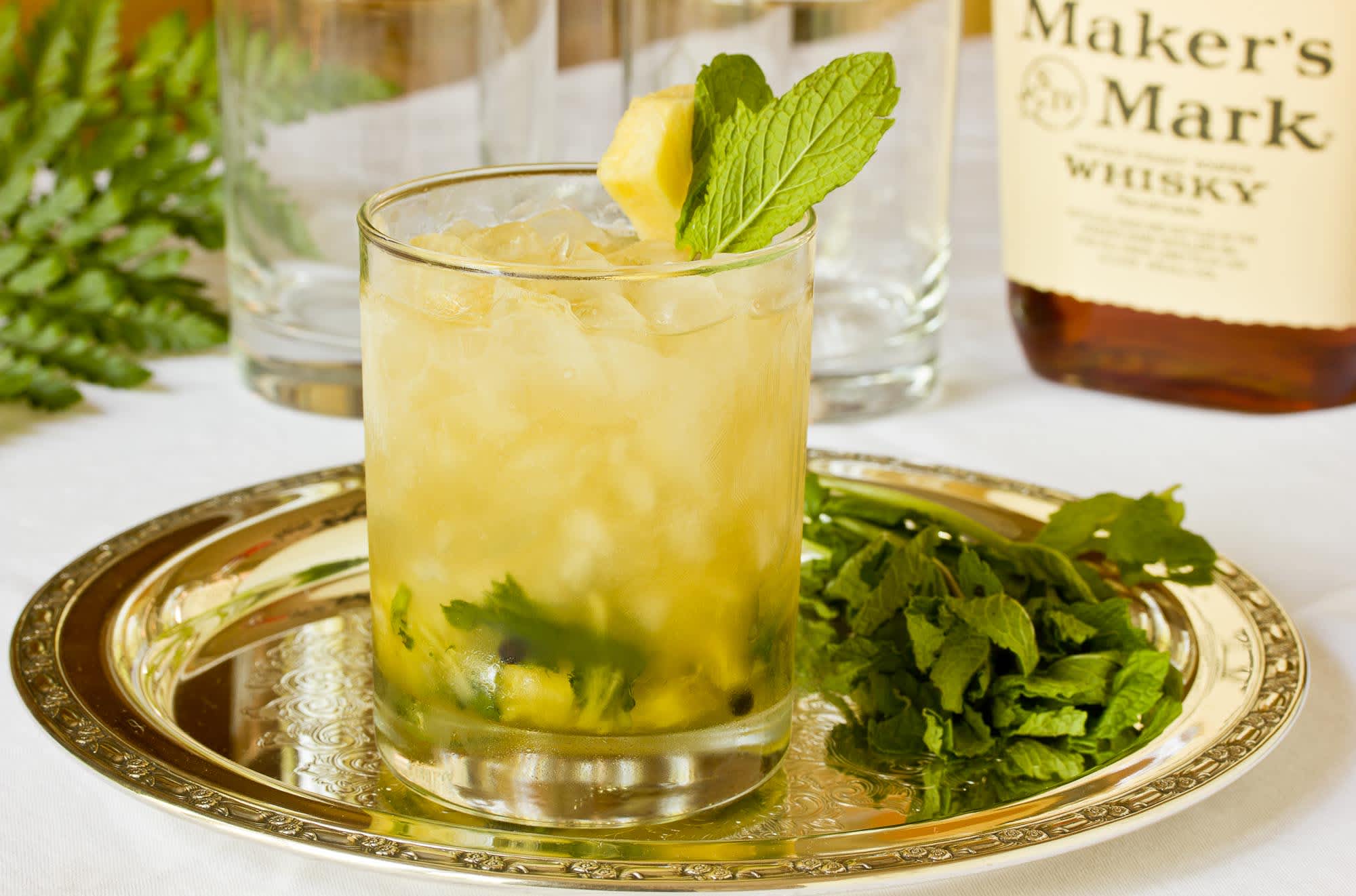 Ginger mint-julep with pineapple cocktail  placed on top of a silver plate with mint leaves and a garland in the background.
