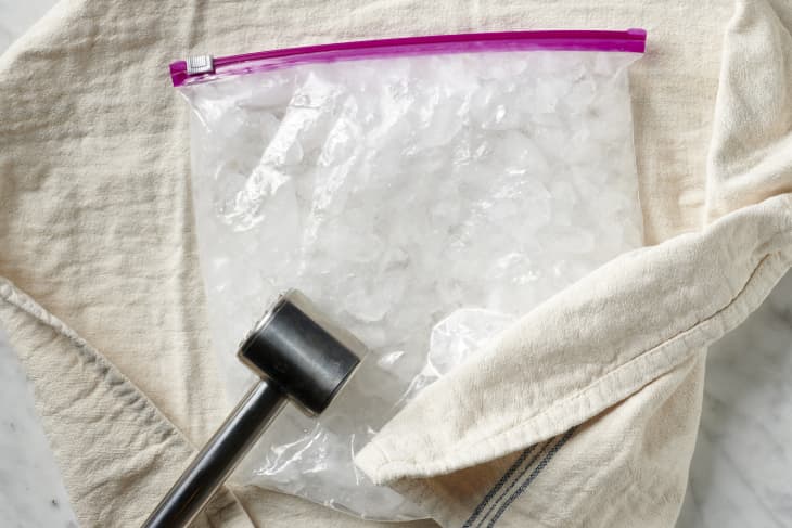 photo of crushed ice on a counter in a zip top bag wrapped in a kitchen towel with a steel mallet