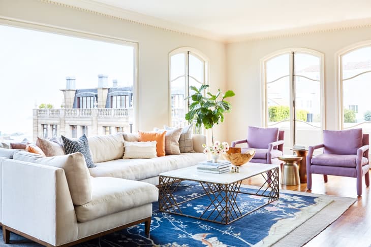 Bright living room with a cream sectional sofa, purple armchairs, blue rug, and a coffee table with decor items.