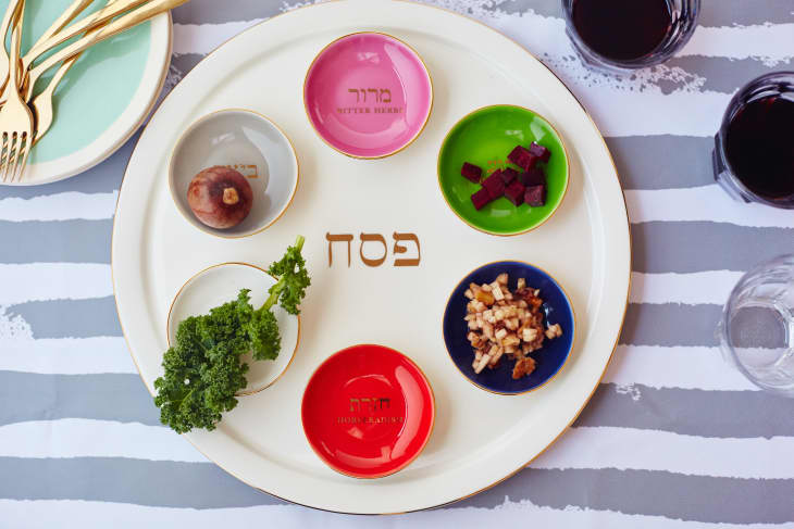 Passover Seder plate with symbolic foods, including parsley, horseradish, and charoset, on a striped tablecloth.