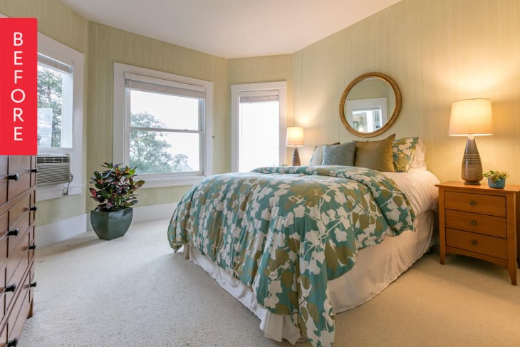 Bedroom with floral comforter, round mirror, two lamps, and a potted plant by the window.