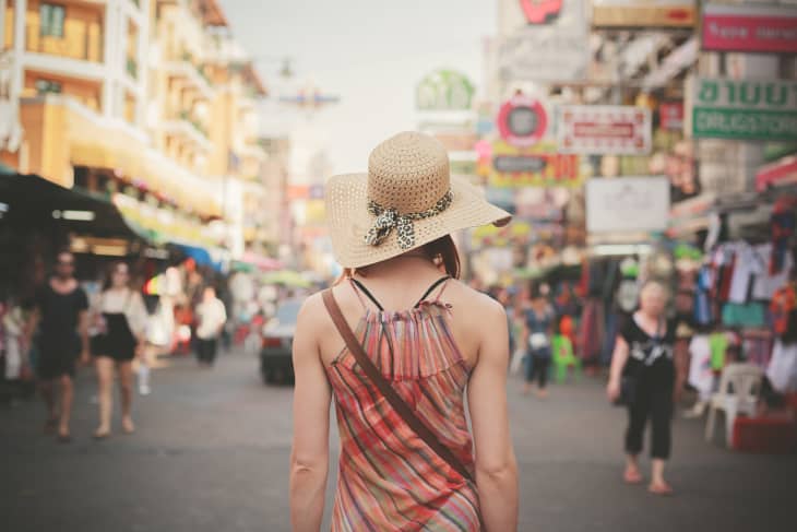 Woman in a straw hat walking through a busy street market with colorful signs and people.