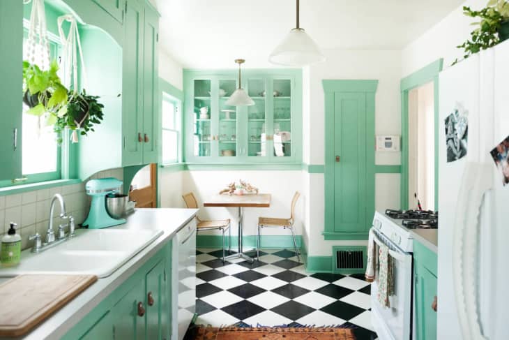 A mint and white galley kitchen with black and white checkerboard flooring