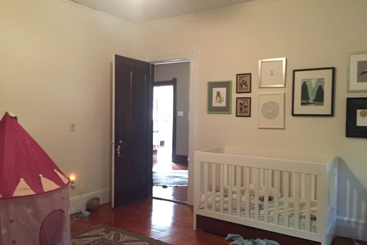 Nursery with a white crib, wall art, pink play tent, and an open door leading to another room.