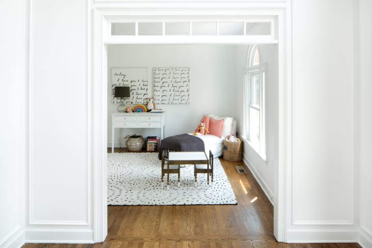 Cozy reading nook with a white chaise, pink pillows, a side table, and a rug with black dots.