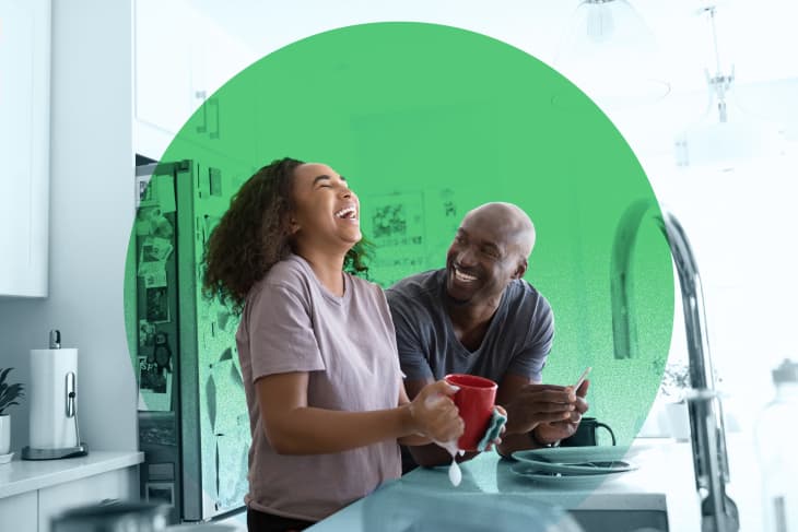 Couple laughing in a kitchen, holding mugs near a sink with a green circle overlay.