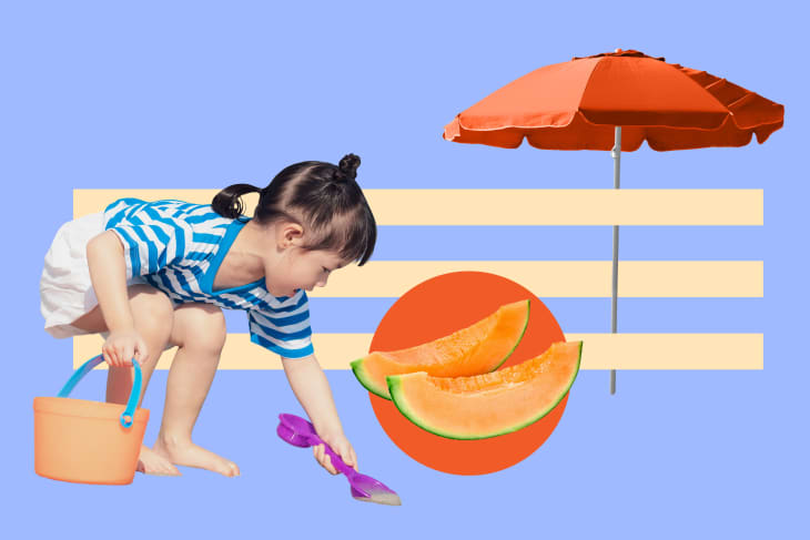 Child in striped shirt playing with sand toys, orange bucket, and slices of cantaloupe under a red umbrella.