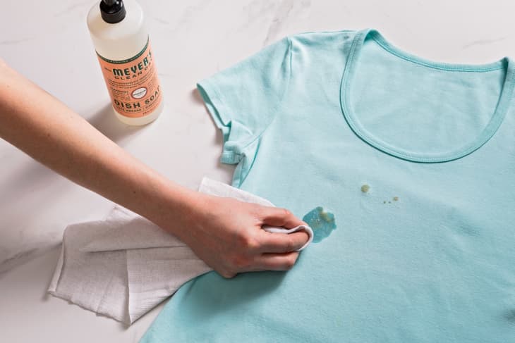 Blotting at a grease stain on a blue t-shirt, with dish soap and a cloth