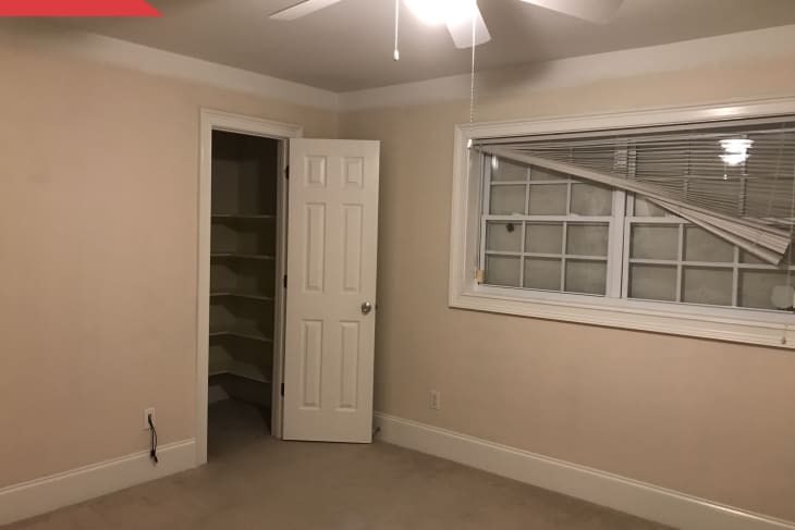 Empty beige room with a ceiling fan, open closet door, and window with bent blinds.