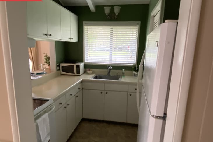 Small kitchen with green walls, white cabinets, a microwave, and a window above the sink.