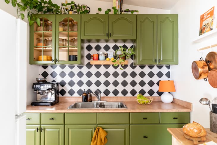 Kitchen with green painted cabinets, a black and white checkered backsplash, and a tan laminate countertop.