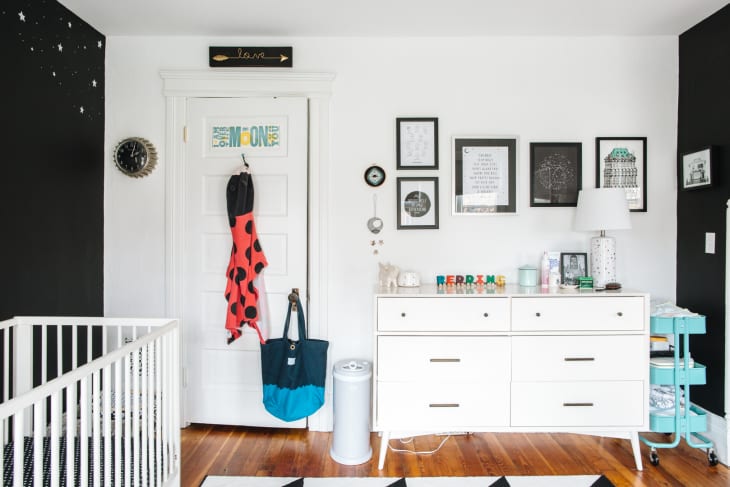 Nursery with black and white walls, crib, dresser, wall art, and colorful decor on dresser.