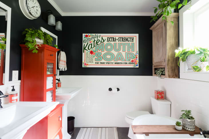 Bathroom with black walls, red cabinet, white sink, plants, and a vintage mouth soap sign.