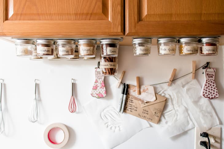 Spices are stored in small jars and affixed with magnets to a strip on the underside of cabinets