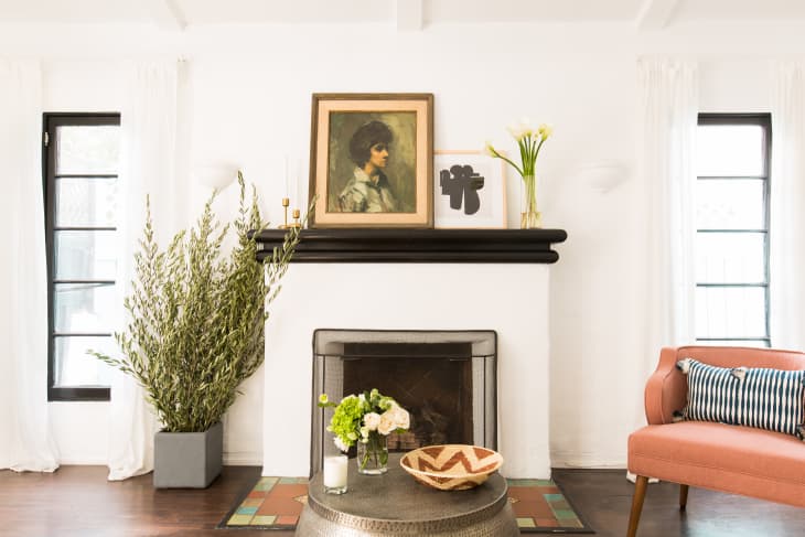 Living room with a black fireplace, portrait painting, potted plant, pink armchair, and decorative bowl on a round table.