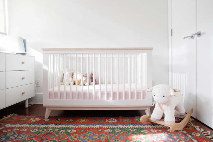 Nursery with a white crib, stuffed animals, colorful rug, dresser, and a plush rocking sheep.