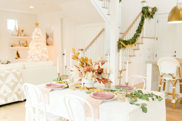 Festive dining room with a decorated table, pink plates, candles, and a Christmas tree in the background.