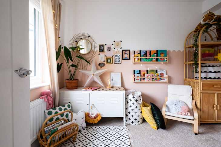 Cozy children's room with bookshelves, a wicker chair, plush toys, and a potted plant near a window.