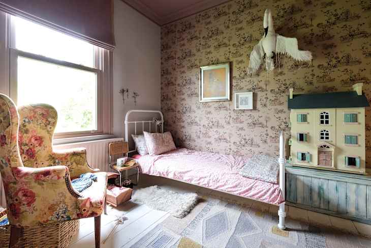 Child's bedroom with floral armchair, single bed, dollhouse, and bird wall decor.