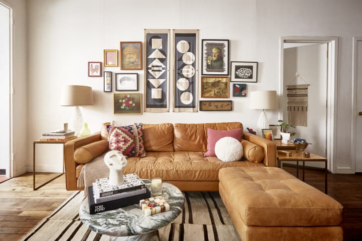 Living room with tan leather sofa, colorful pillows, gallery wall art, marble coffee table, and wooden floor.
