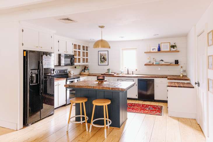 Spacious kitchen with wooden countertops, black appliances, island with stools, and red rug on light wood floor.