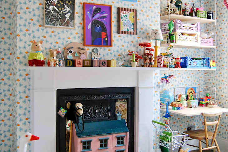 Colorful playroom with a white mantel, decorative toys, artwork, and a small table with chairs.