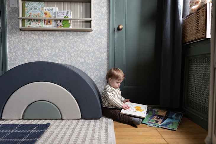 Toddler holding a book on wood floor in wallpapered playroom