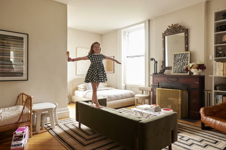 A child stands on a green couch in a studio apartment.
