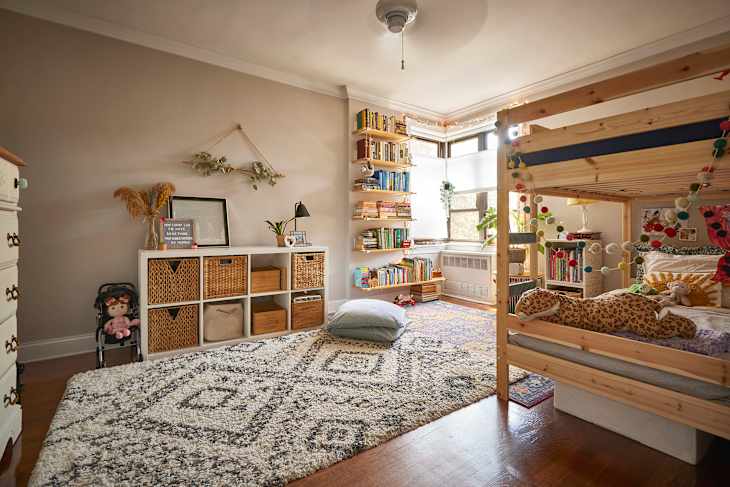 Bunk beds in bedroom with cube storage, books on shelves, and layered area rugs.