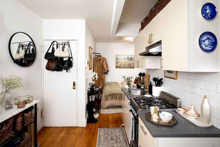 Cozy kitchen area with a round mirror, hanging bags, and a small dining space featuring a green blanket and decorative plates.