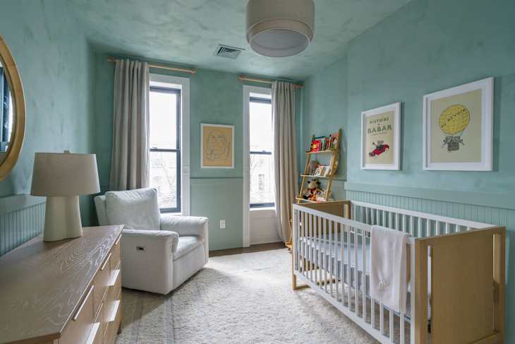 Nursery with light blue walls, a white crib, a cozy armchair, and framed children's artwork.