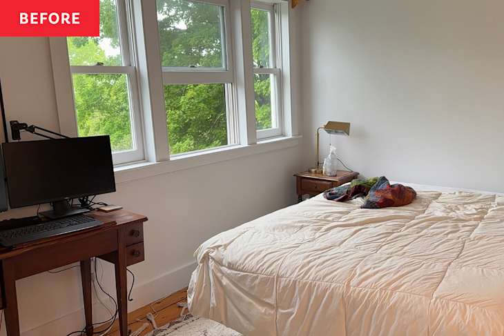A bright bedroom featuring a bed with a cream comforter, a wooden desk with a monitor, and a bedside table with a lamp.