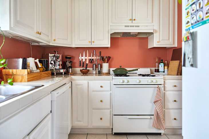 Cozy kitchen with white cabinets, a green pot on the stove, and various kitchen tools displayed on the wall.