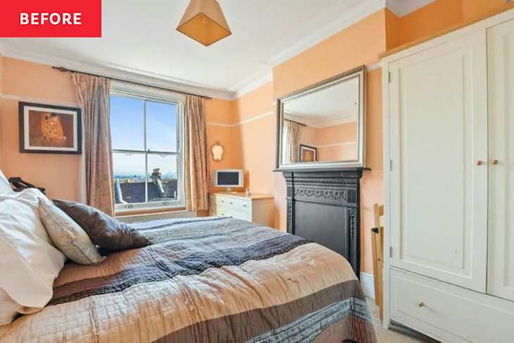 Cozy bedroom with a large window, orange walls, a quilted bedspread, and a decorative fireplace.