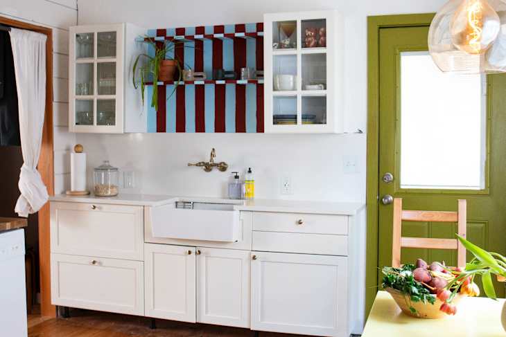 Bright kitchen with white cabinets, colorful striped shelves, a farmhouse sink, and a bowl of vegetables on the table.