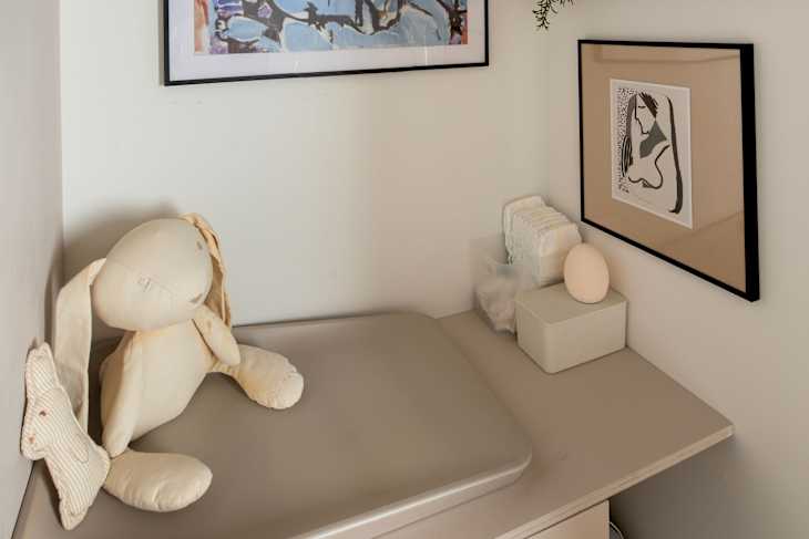 A corner with a framed portrait, a shelf with photos, a plush bunny, and a changing table with supplies.