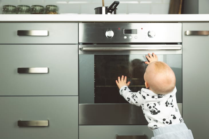 Baby reaching for a stainless steel oven in a modern kitchen.