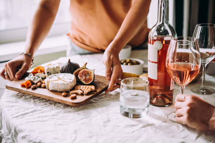 Person sets down appetizer cheese board at a dinner party