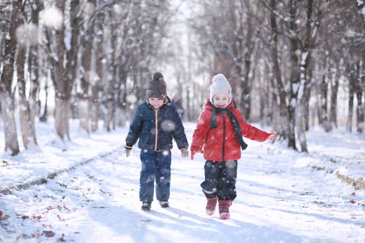 Two children in winter jackets run in the snow