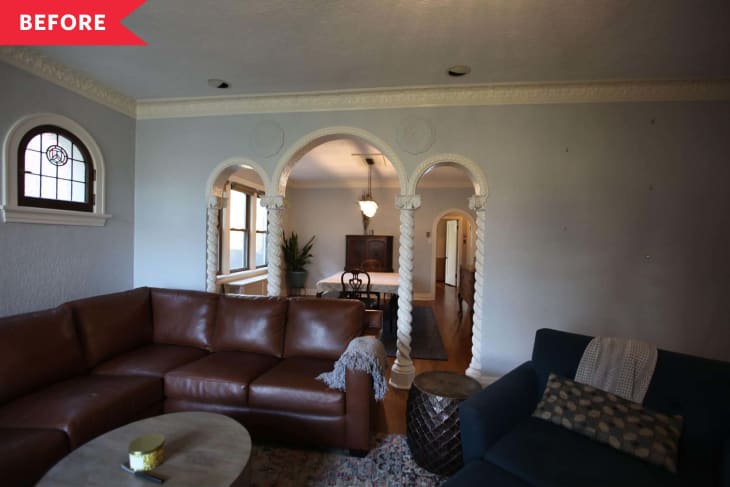 Living room with brown leather sectional, blue armchair, and arched entryway to dining room with ornate columns.
