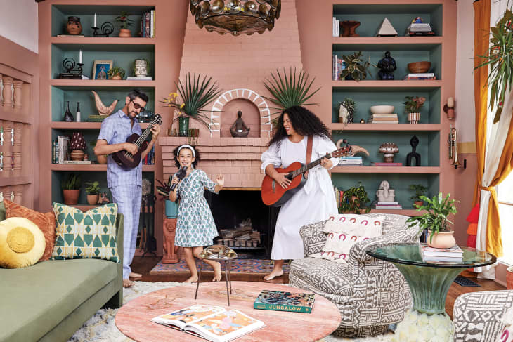 Family playing music in a colorful living room with guitars, bookshelves, and patterned furniture.