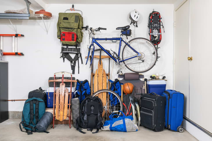 Garage storage with a blue bike, backpacks, sleds, a basketball, and suitcases neatly organized against a wall.
