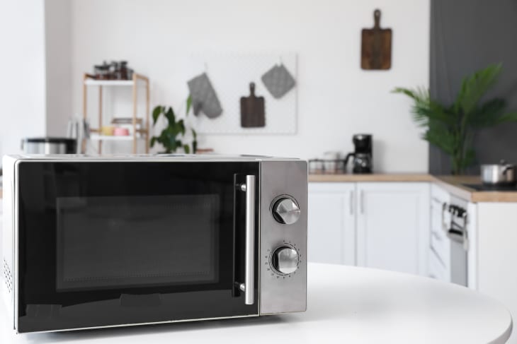 Stainless steel microwave on a white countertop in a modern kitchen with plants and wooden accents.