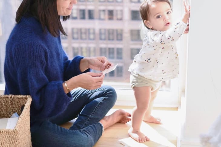 Woman in blue sweater sitting on floor with toddler, surrounded by fabric swatches near a window.
