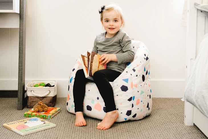 Child sitting in a Big Joe Milano Kid’s Chair in Terrazo pattern. Some books around
