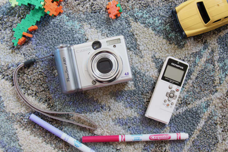 Vintage digital camera beside vintage voice recorder with toys and markers around.
