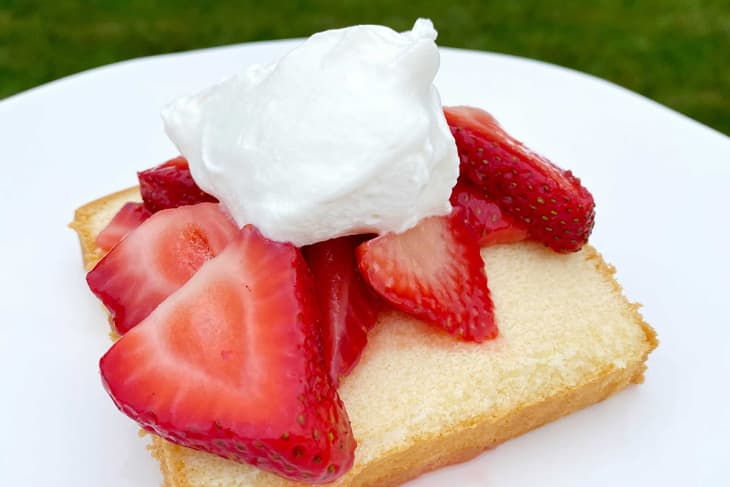 Slice of pound cake topped with fresh strawberries and whipped cream on a white plate.