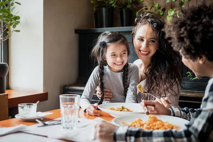Family enjoying a meal together at a wooden table with plants in the background.