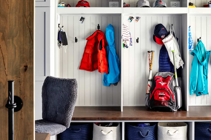 Mudroom with open lockers, red and blue jackets, baseball gear, hats, and woven baskets on lower shelves.