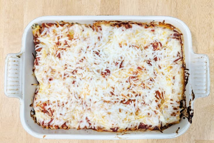 Baked lasagna with melted cheese in a white rectangular dish on a wooden table.